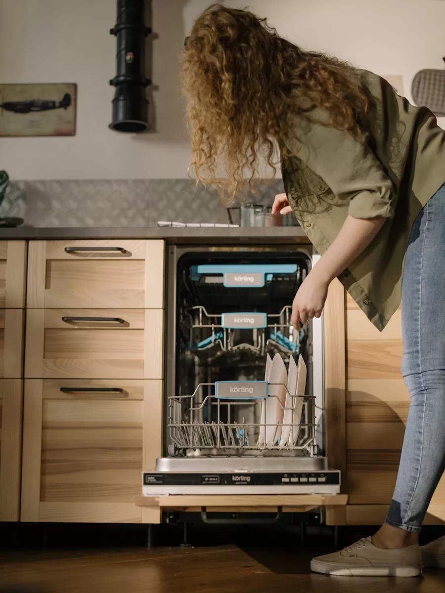 A woman loads dishes into a modern automatic dishwasher in a stylish kitchen setting.