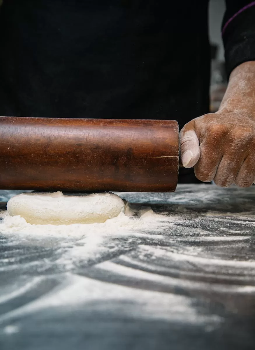 Close-up of a chef rolling dough with a wooden pin, capturing the art of baking.